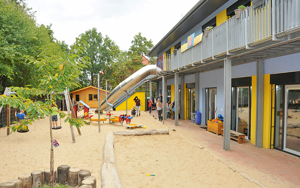 Das Außengelände der Kita Kinderzeit mit großer Sandfläche und Spielgeräten
