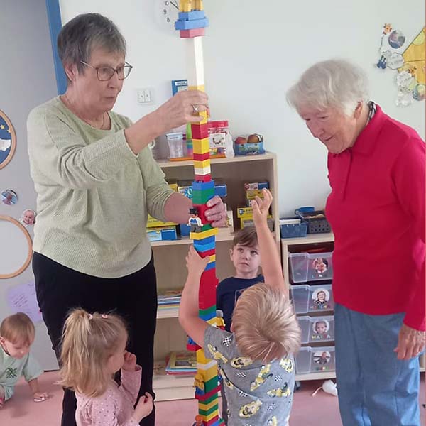 Drei Kita-Kinder bauen mit zwei Seniorinnen einen Lego-Turm.