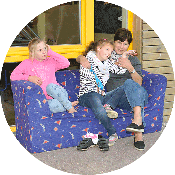 Nachmittagsbetreuung, zwei Kinder und und eine Erzieherin sitzen auf einem Sofa im Freien